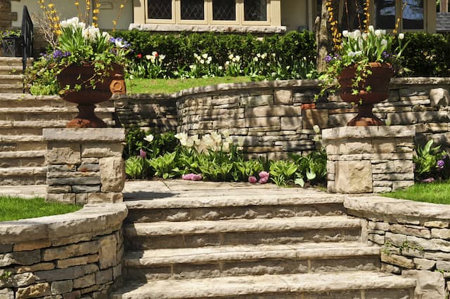 stairs and retaining walls made our natural tan stone in a yard with lush landscaping featuring colorful flowers.